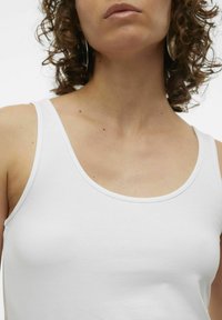 Witte tanktop met een ronde hals. Het heeft een gladde, katoenen textuur en dunne bandjes, wat de eenvoudige en minimalistische vormgeving benadrukt.