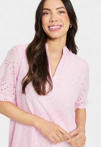 Blouse rose avec broderie œillet, manches courtes bouffantes et col mandarin. Tissu léger avec motifs floraux et texture subtile.