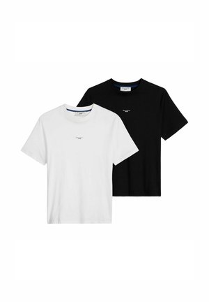 Uomo che indossa una t-shirt nera Marc O'Polo Denim a maniche corte e jeans azzurri chiari, con una mano in tasca, ritagliato al collo e ai fianchi.