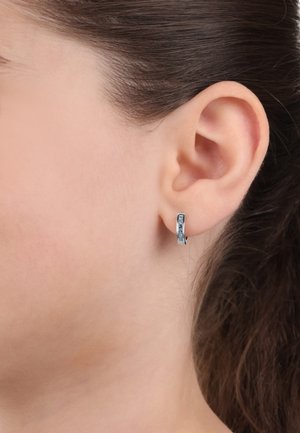 Orecchini a cerchio in argento con una finitura testurizzata, caratterizzati da piccole gemme blu incastonate lungo la parte anteriore; progettati per aderire strettamente al lobo dell'orecchio.
