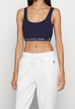Femme portant un crop top bleu marine avec une bande logo « Polo Ralph Lauren » et un pantalon de survêtement blanc à cordon avec un petit logo joueur de polo sur la hanche.
