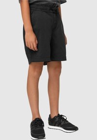 Shorts noirs avec une taille élastique, présentant une coupe décontractée et des poches latérales. Associés à des baskets noires. Texture de tissu lisse.