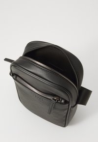 Czarna torba crossbody z teksturowanym przodem, skórzanymi akcentami i zapięciem na zamek. Posiada kompaktowy kształt kwadratowy i mocny pasek.