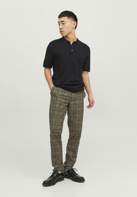 Sort kortærmet polo skjorte med krave, parret med beige og grønternet bukser. Modellen har sorte snørresko på.