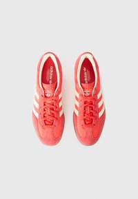 Røde Adidas sneakers med en glat overdel, hvidt tre-stribe design og teksturerede snørebånd. Polstring i sålen for komfort.