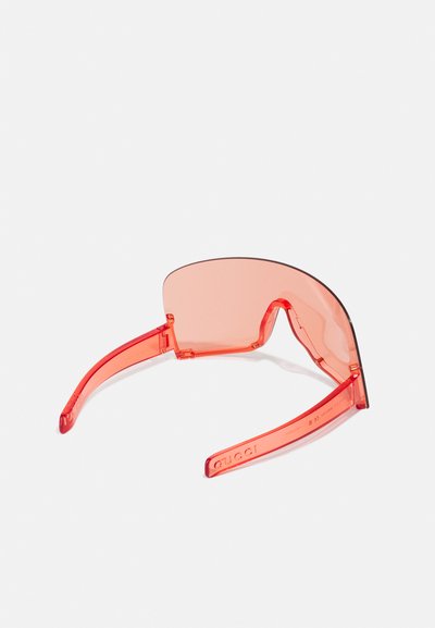 Gafas de sol rojas transparentes con lentes grandes y curvados y brazos gruesos. La montura es brillante con una textura suave, con un sutil branding.