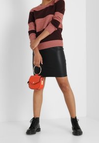 Pasiasty różowo-bordowy sweter, czarna skórzana spódnica, czarne sznurowane botki i mała czerwona torebka z okrągłym uchwytem.