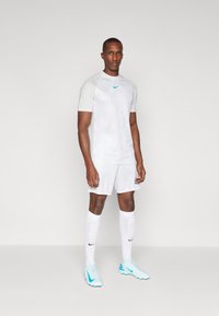White athletic jersey with short sleeves and a light blue Nike logo, paired with matching shorts, white socks, and light blue soccer cleats.