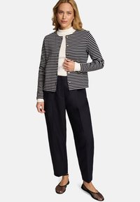 Cardigan rayé bleu marine et blanc, avec un col rond et des boutons dorés, associé à un pantalon large noir et des ballerines en mesh.