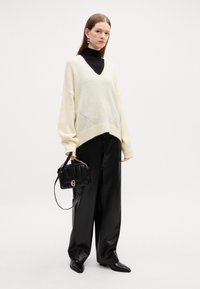Maglione oversize crema con scollatura a V e orlo a coste, abbinato a pantaloni in pelle nera a vita alta. Borsa nera con accentuazione a catena.