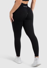 Zwarte leggings met een hoge tailleband, gemaakt van rekbare, gladde stof. Sluit nauw aan op het lichaam met subtiele stikdetails. Te combineren met witte sneakers.