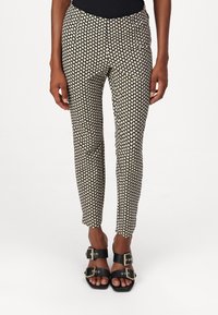 Zwarte en crèmekleurige, gemusterde broek met een slim fit, met een hartmotief en steekzakken, gecombineerd met zwarte sandalen met open tenen en gespen.