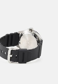 Montre à bracelet en silicone noir avec un boîtier en acier inoxydable. Dispose d'un bracelet texturé et d'une boucle en acier poli. Dos gravé avec des détails.