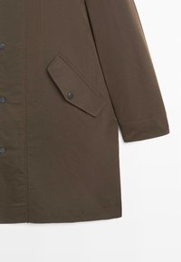 Brązowa kurtka wierzchnia z zapięciem na guziki, skośną klapką kieszeni i gładką fakturą. Końce rękawów są wykończone mankietami.