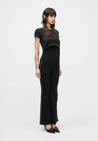 T-shirt nera corta abbinata a pantaloni neri a zampa con dettagli laterali. La modella indossa décolleté nere con punta appuntita.