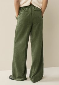 Wide-leg, olive green corduroy pants with a textured finish, featuring an elastic waistband and two back pockets.