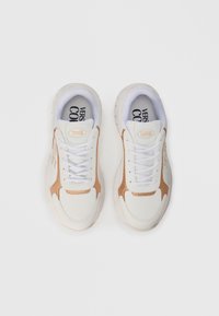White sneakers with beige suede accents, round toe, white laces, and a thick textured sole. Features branding on the tongue and insole.