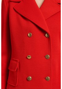Czerwony, dwurzędowy płaszcz wykonany z teksturowanej tkaniny, z dużymi złotymi guzikami i boczną kieszenią z klapką.