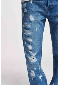 Ausgewaschene blaue Jeans aus Denim mit verschiedenen ausgefransten Rissen und hellen Wascheffekten; mit lockerem Sitz und sichtbaren Taschen.