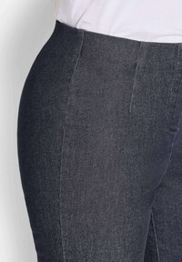 Close-up van donkergrijze slim-fit broek gedragen met een ingestopte witte shirt, waarbij de textuur van de stof en details van de voornaad zichtbaar zijn.