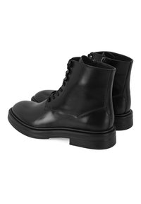 Zwarte leren enkellaarsjes hebben een gladde afwerking, een ronde neus, vetersluiting aan de voorkant en een verhoogde, gestructureerde rubberen zool met een ritssluiting aan de achterkant.