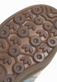 Rūpnieku zole ar brūnu teksturētu rakstu, kas ietver apļveida un lapu formas, nodrošinot saķeri un vilkmi ar nelielu spīdumu.