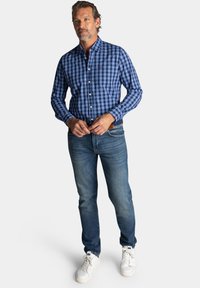 Blauw en witte geblokte shirt, met knopen, lange mouwen. Gecombineerd met blauwe jeans en witte sneakers. Eenvoudige, casual look.