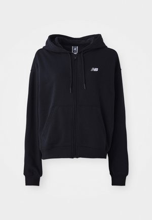 Haut à zip noir en tissu doux, avec une poche kangourou, un capuchon à cordon de serrage et un petit logo réfléchissant sur la poitrine.
