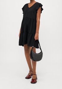 Svart lager-på-lager klänning med volangärm, matchad med en svart handväska med silvernitar och röda lackskor med ankelremmar.