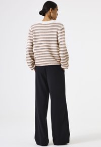 Jersey a rayas en color crema con líneas negras y rosas, con un cuello redondo y corte holgado, combinado con pantalones anchos negros.