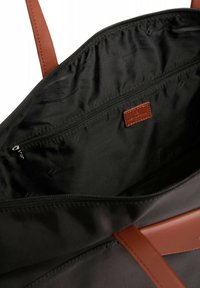 Interno nero di una borsa a spalla con una tasca con zip, dettagli in pelle marrone e etichetta del marchio. Texture liscia e forma strutturata.