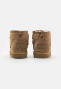 Botines de ante marrón con un suave forro interior, que cuentan con una etiqueta de marca en el lado exterior y una suela de goma resistente.