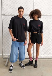 Svart kortermet T-skjorte med rødt leppelogo; denim culoter; svarte innpakningsshorts; rosa tie-dye sokker; svarte støvler; uformell urban stil.