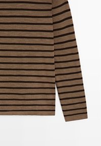 Chemise à manches longues marron avec des rayures noires horizontales uniformément espacées, présentée à plat avec la manche droite étendue.