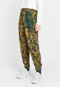 Geweckte cargo broek met bloemenpatroon in geel en groen, met elastische boorden en een tailleband; beschikt over opgestikte zakken en een mix van texturen.