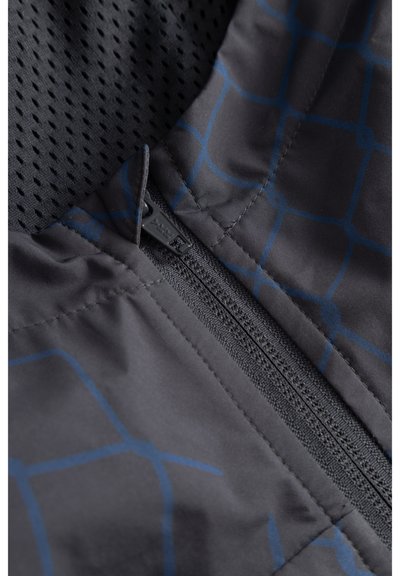 Gros plan sur une fermeture éclair noire sur un tissu sombre avec un motif à grille bleue subtile et une doublure noire perforée en dessous.