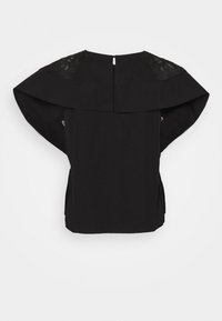 Haut noir à manches courtes avec un large col style cape et des détails en dentelle sur les épaules, vu de dos sur un fond uni.