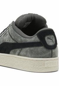 Sneaker grigio in suede con dettagli neri e suola in gomma. Presenta una linguetta posteriore testurizzata, logo Puma e cuciture a contrasto. Design a metà caviglia.