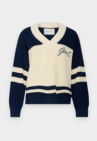 Tmavě modrý a krémový pletený svetr s výstřihem do V, zdobený pruhovanými vzory a vyšitým logem na hrudi. Volný střih s žebrovanými manžetami.