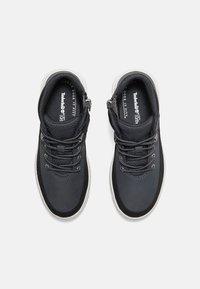 Svarta sportskor med textilmaterial och släta läderöverdrag. Har grå snören och gummisulor, med en dragkedja på sidan.