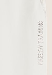 Pantalones jogger de tela blanca con una textura suave, que presentan un diseño de brillantes piedras de imitación formando la palabra "REBEL" de forma vertical en el costado.