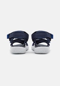 Mer navy siniset urheilu sandaalit, joissa on säädettävät hihnat, pehmustettu pohja ja valkoinen kumipohja, jossa on teksturoitu pito.