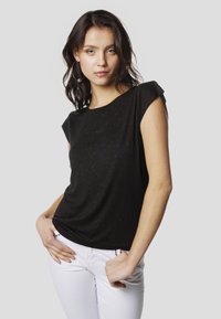 Melnas, īsām piedurknēm top ar mīkstu tekstūru un smalku mirdzošu rakstu. Saskaņots ar baltām biksēm, uzsverot ikdienišķu stilu.