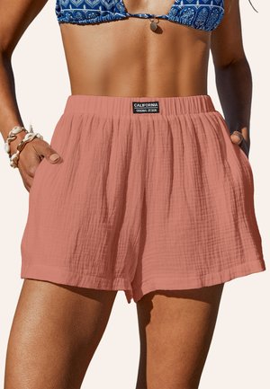 Shorts de couleur pêche avec un tissu léger et texturé. Dispose d'une taille élastique et de poches latérales, étiquetées "CALIFORNIA" sur la taille.
