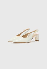 Valkoiset patenttinateksiset slingback-korkokengät, joissa on terävät varpaat, neliön muotoiset korkohait ja sivun solkiyksityiskohta. Sujuva pinta ja minimalistinen muotoilu.