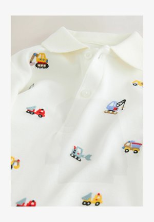 Hvid polo-shirt med broderede farverige byggemaskine-motiver, herunder gravemaskiner og lastbiler. Blødt bomuldsstof og klassisk krave.