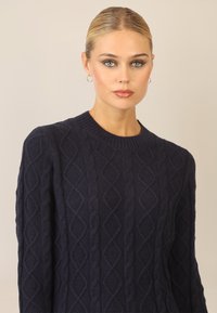 Marineblauer Kabelstrickpullover mit Rundhalsausschnitt, der ein strukturiertes Rautenmuster und gerippte Bündchen aufweist, entworfen für eine körpernahe Passform.