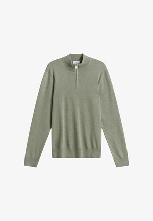 Langærmet, lyseolivengrøn sweater med ribstrikket høj hals og halvlukning med lynlås foran på hvid baggrund.