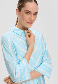 Himmelblaues Hemd mit weißen und rosa vertikalen Streifen, mit Kragen und 3/4-Ärmeln, weicher Textur und Knopfdetail am Bündchen.