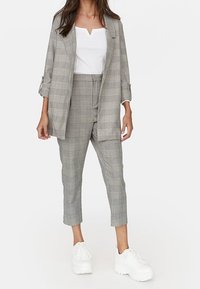 Costume à carreaux gris avec une veste décontractée et un pantalon cropped, porté sur un haut blanc, associé à des baskets blanches imposantes.